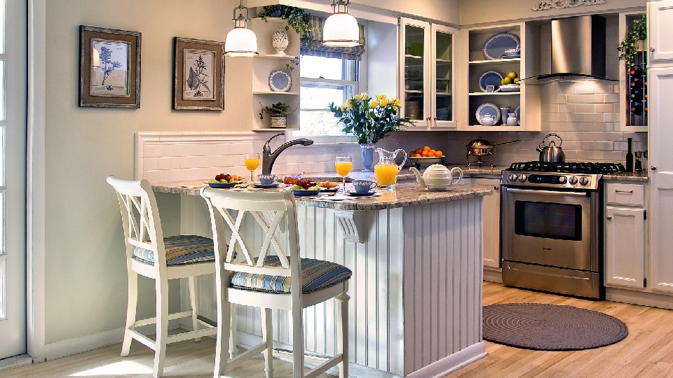 A white kitchen with wooden coutertop, chairs & pendant lights