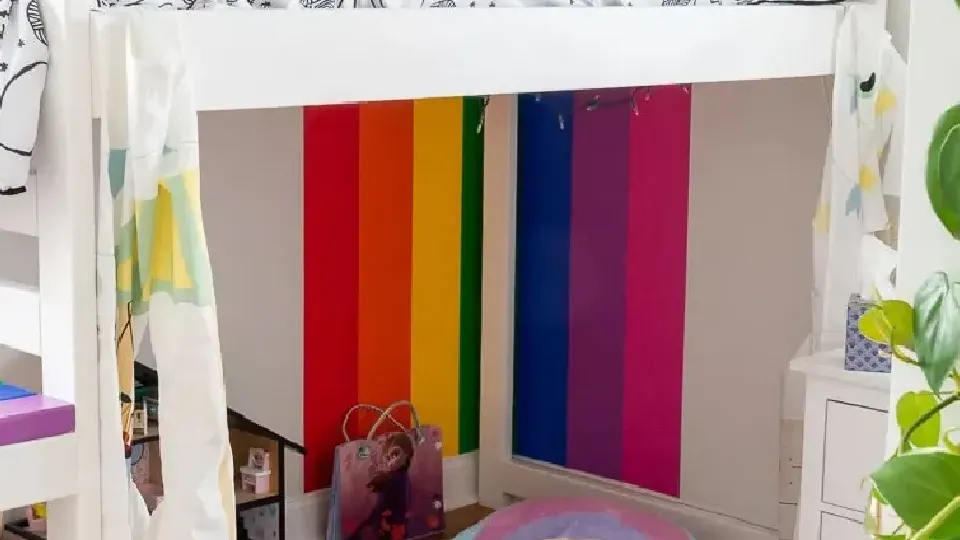 A kids room with a cute bed and rainbow stripes on wall