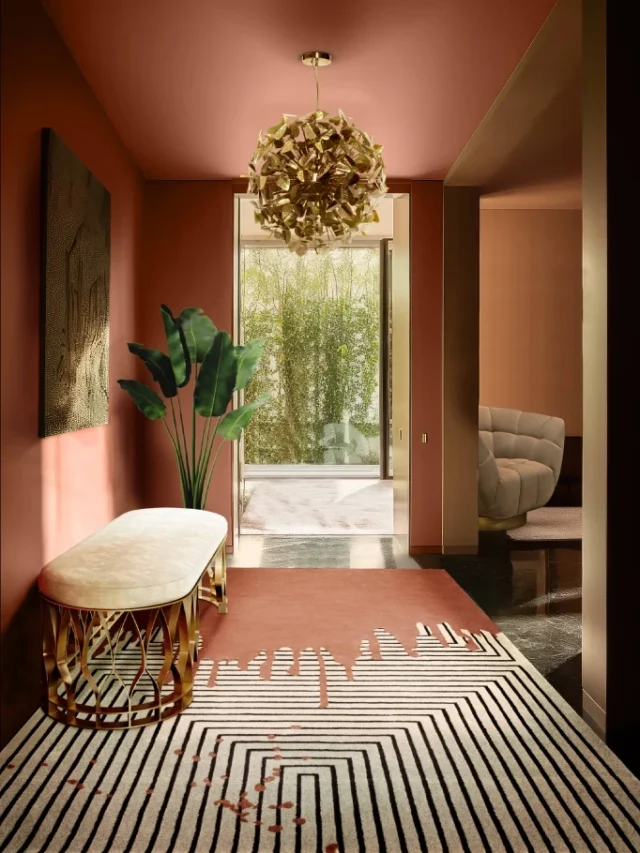 A pink hallway with painting on the wall, patterned rug in the center, indoor plant and couch next to the wall