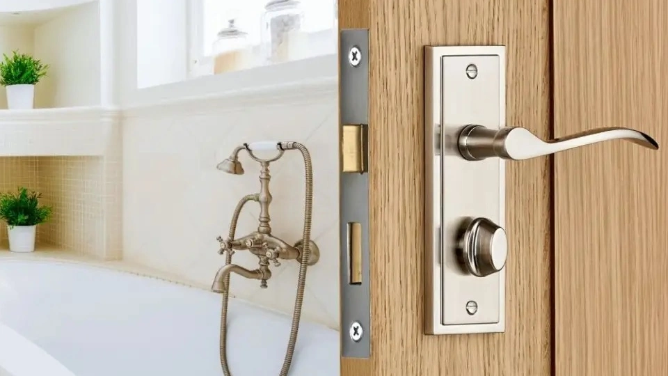 a metal finished mortise doorknob with lock over a wooden door for bathroom