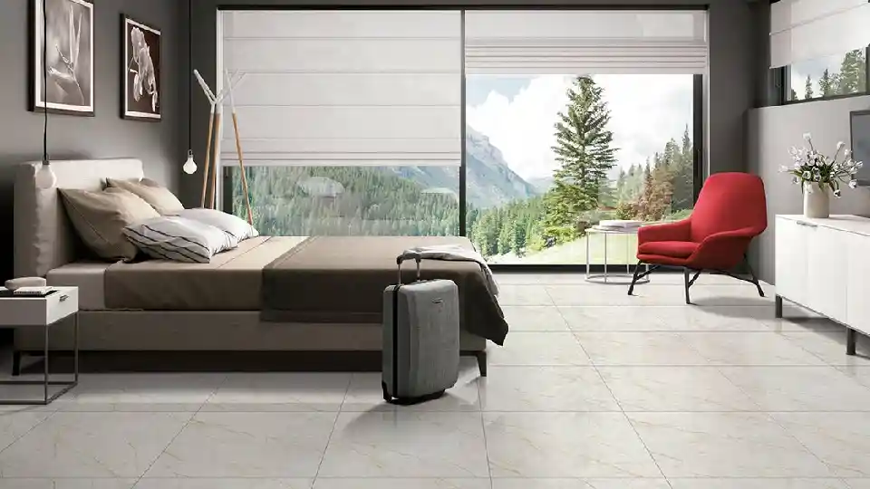 Matt tiles in a bedroom setting, king size bed with grey beddings, grey trolley bag on the floor, red chair and floor to ceiling glass window
