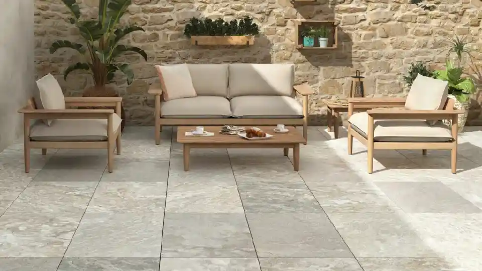 Matt tiles in an outdoor setting with 4 light-grey seater sofa set with potted plant and hanging shelves on a light brown wall
