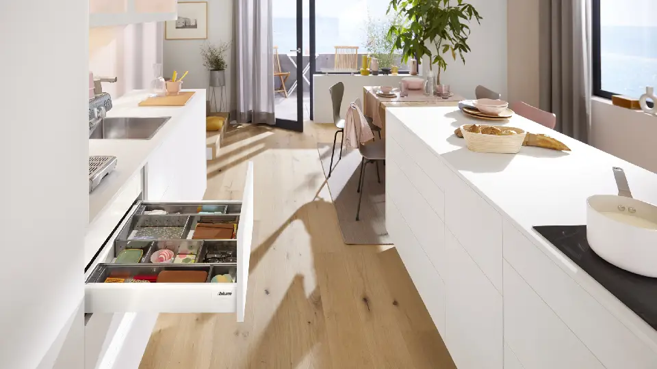 brown wooden floors in a kitchen with white cabinets , counters and drawers