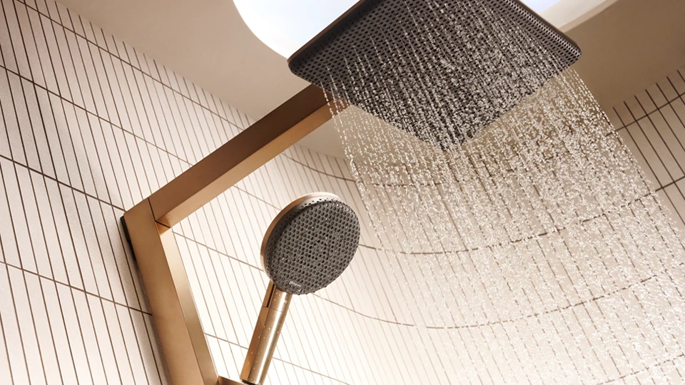 Award winning premium Gold-toned Hansgrohe Raindance Alive shower systems with square overhead rain shower and round handheld shower, mounted on tiled bathroom wall.