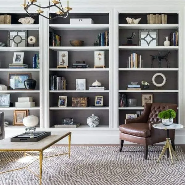 white floor-to-ceiling bookcase, books and articles arranged, room setting, leather sofa, wooden table, chandelier, small plant