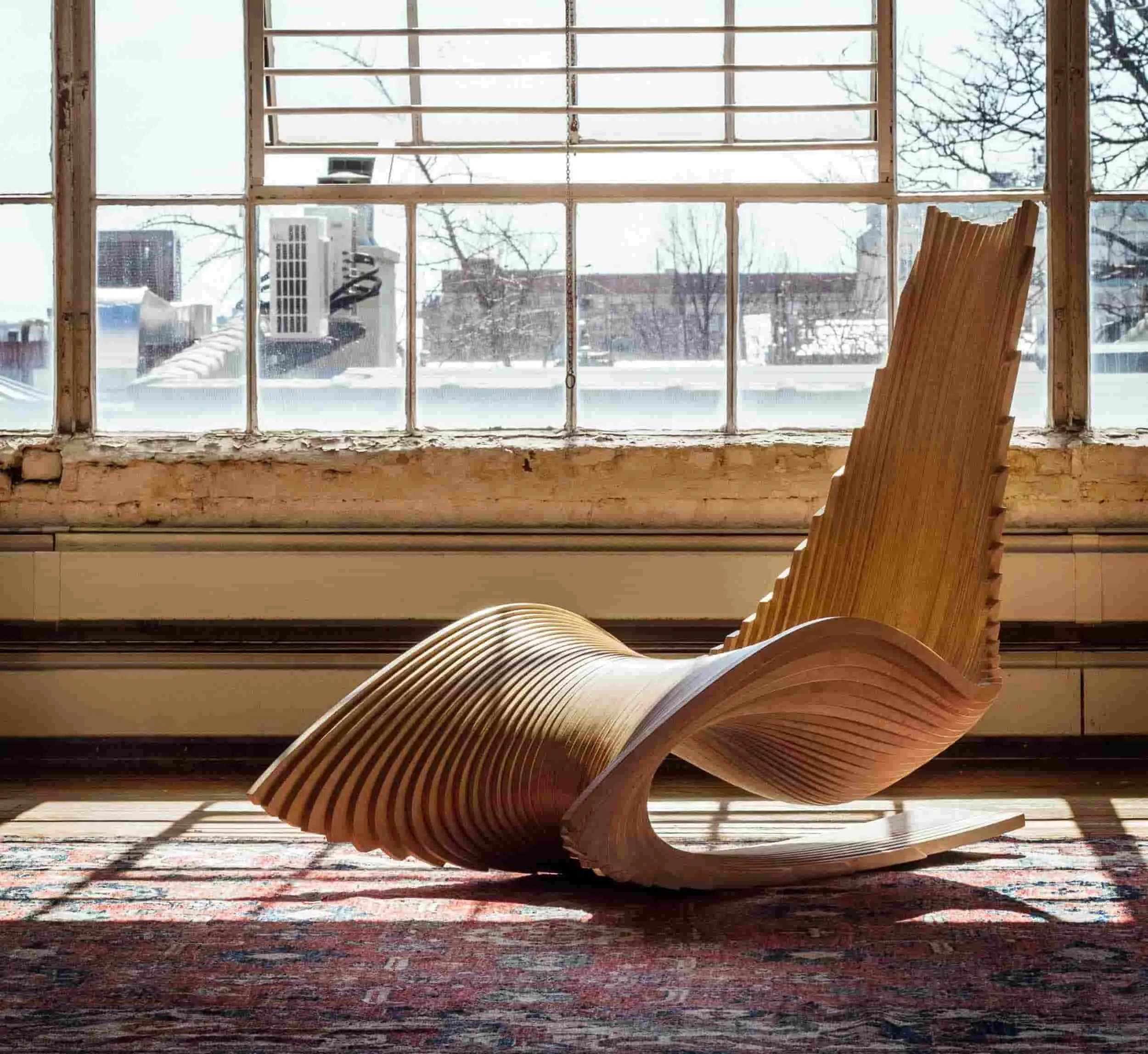 Elegant yet unique piece in light brown color placed on a multicolored rug with a window showcasing a brilliant view of the outside.