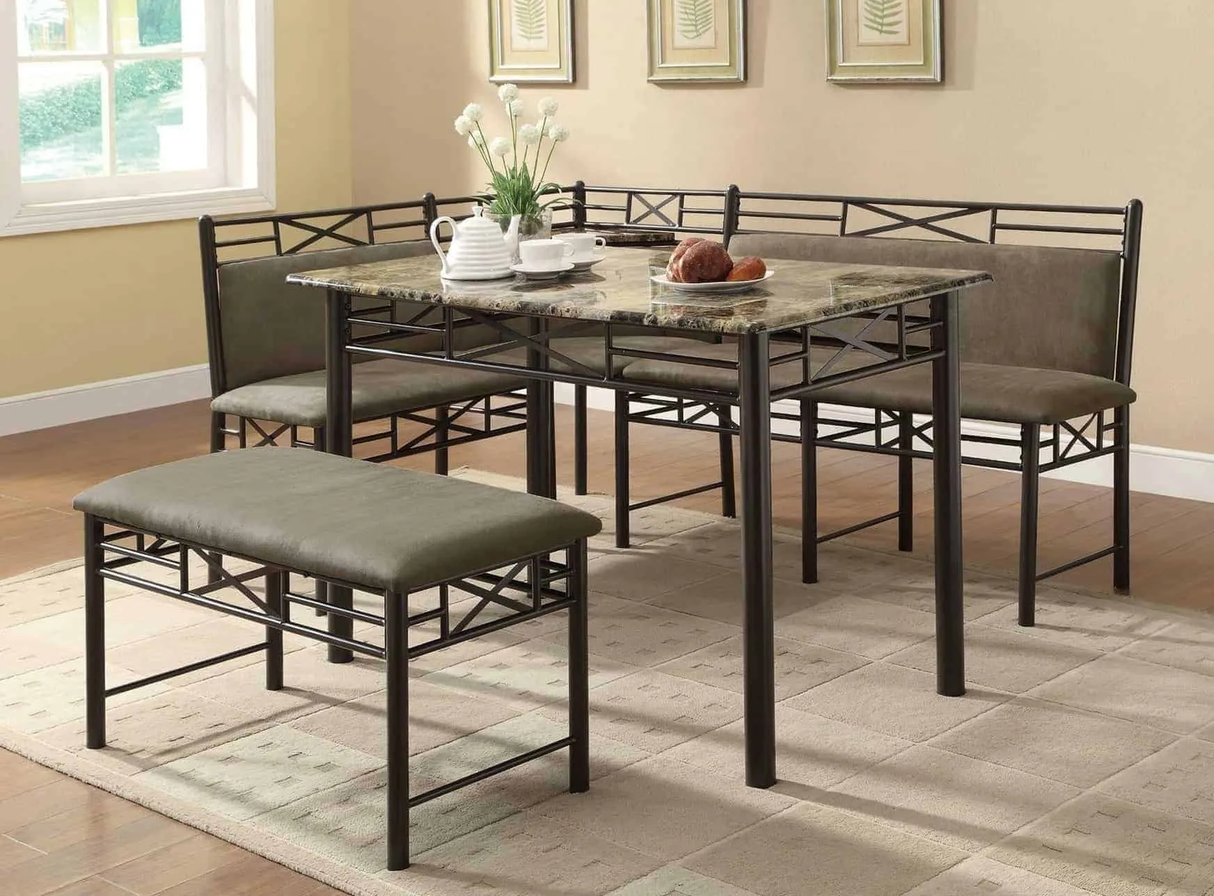 multicoloured ganite top dining table with a wrought iron frame, bench and seats with gray cushions, in a room with a window and light orange walls.