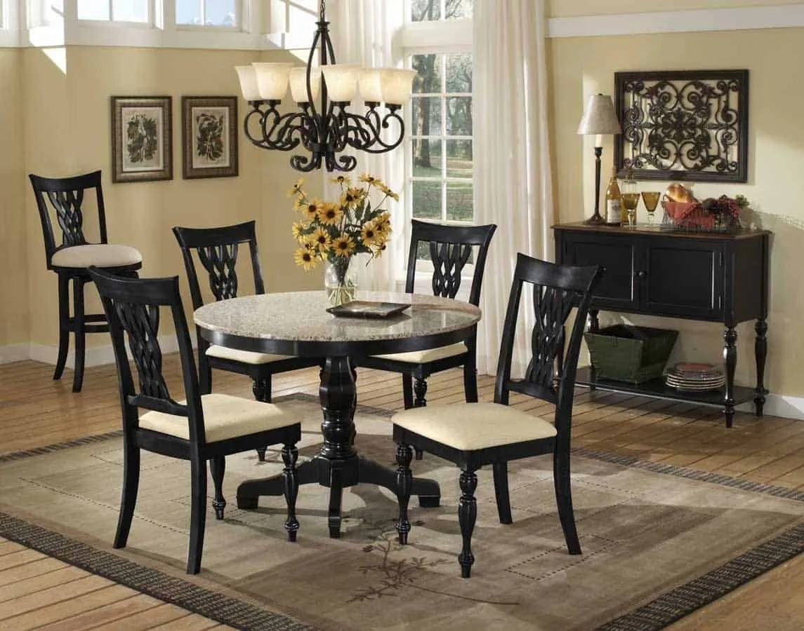 granite top dining table with black wooden base, black wooden chairs with off-white cushions, in a room with a chandelier and other wooden furniture, a wooden flooring with a rug