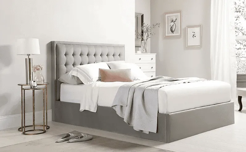 double bed with grey headboard and frame, white pillows and bedsheet, white walls, sandals, wall hangings