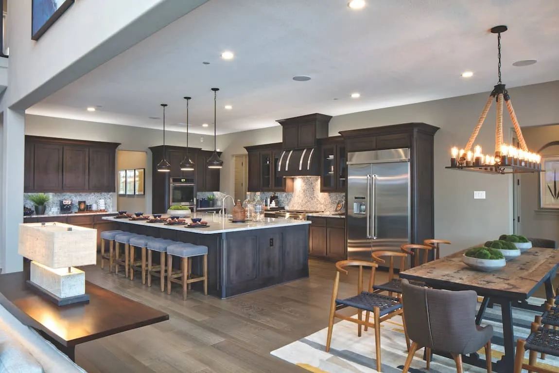 modern fully accessorized brown wooden floored kitchen with lamps, with a dining table, lamps and kitchen appliances