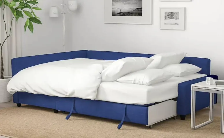 white and blue sofa bed, white pillows, white walls with hangings, indoor plant, white side table