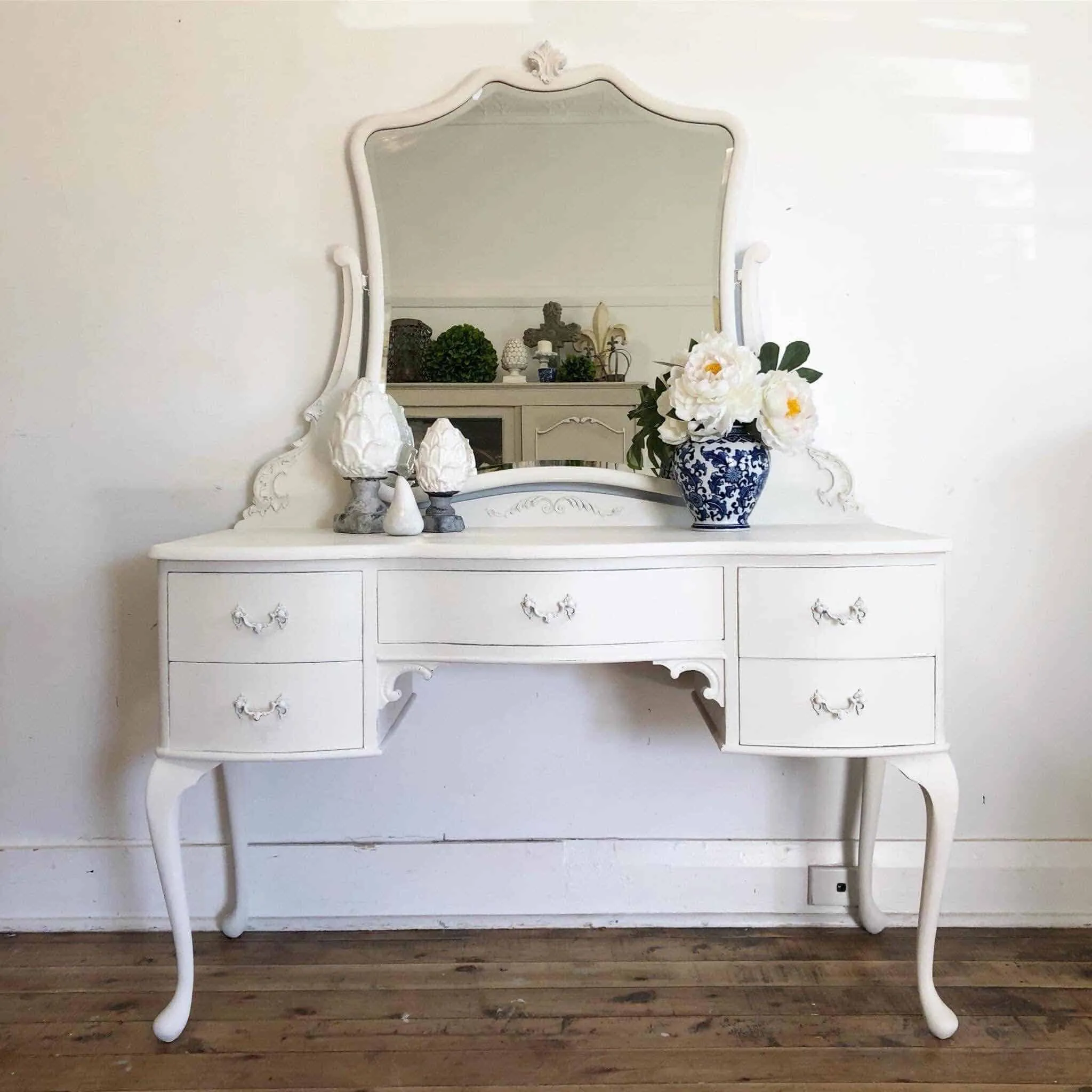 A classic white-colored vanity design with an irregular-shaped mirror and good storage space, kept in a white-colored room.