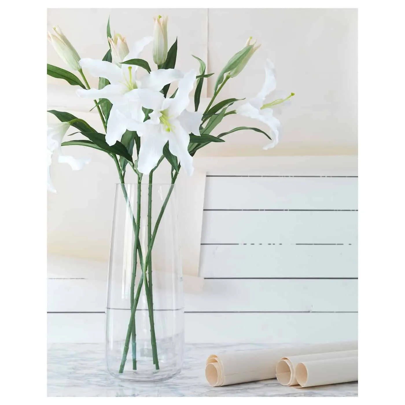 White lily flowers in a glass vase with green foilage