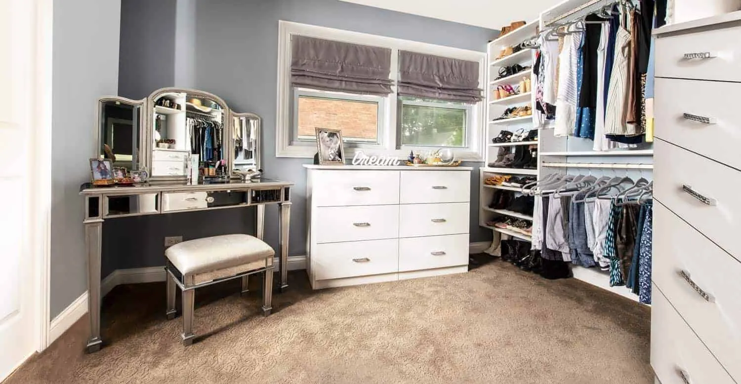 walk-in closet vanity withan ottoman and a a white chest of drawers