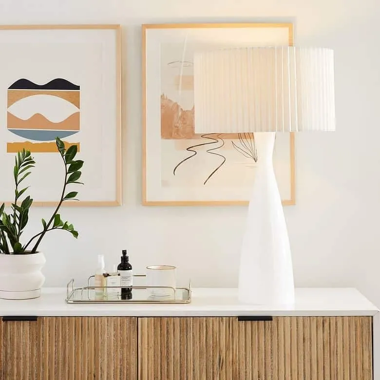 white lamp on a table with plant and paintings