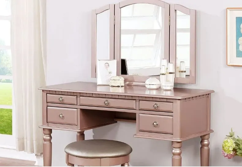 blush pink vintage vanity with a tri-fold mirror and metallic knobs