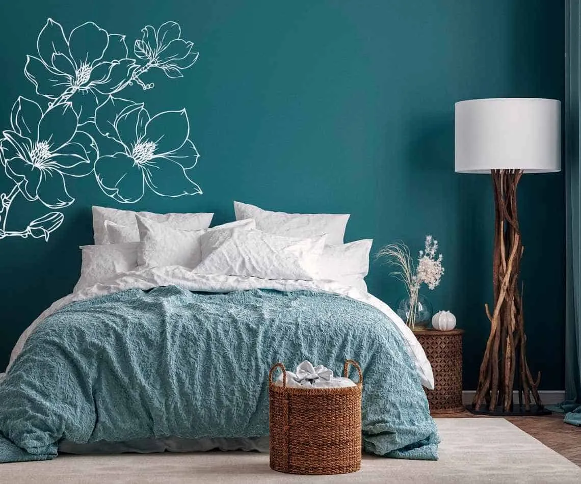 blue bedroom wall with white floral sticker, a bed and a lamp