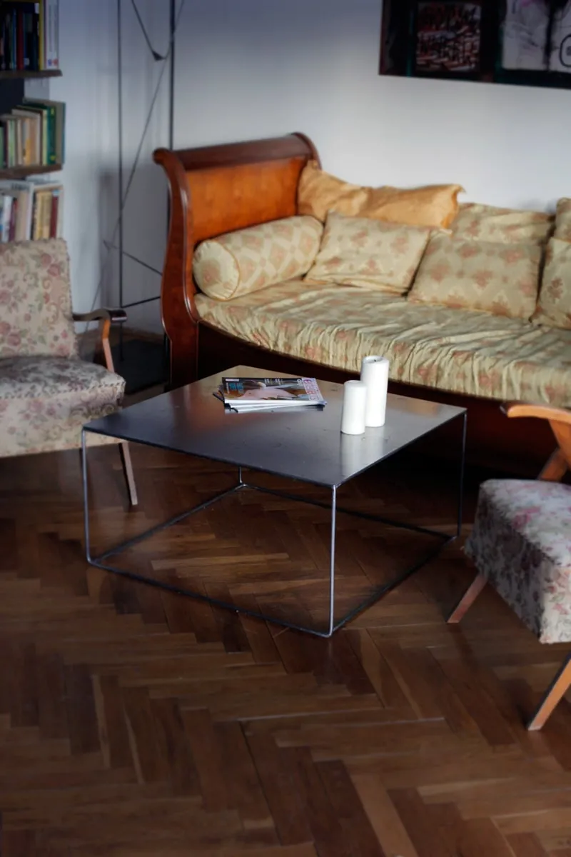 all metal centrepiece, with sleek metal legs, wooden flooring, yellow coloured sofa and cushions, wooden sofa, bookshelf, books, magazines, white walls