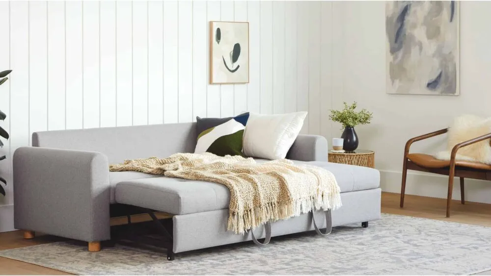grey Pull out lounge in living room, comfortable seating area, cushions, grey carpet, white walls, painting hanging on wall, side table, vase on side table