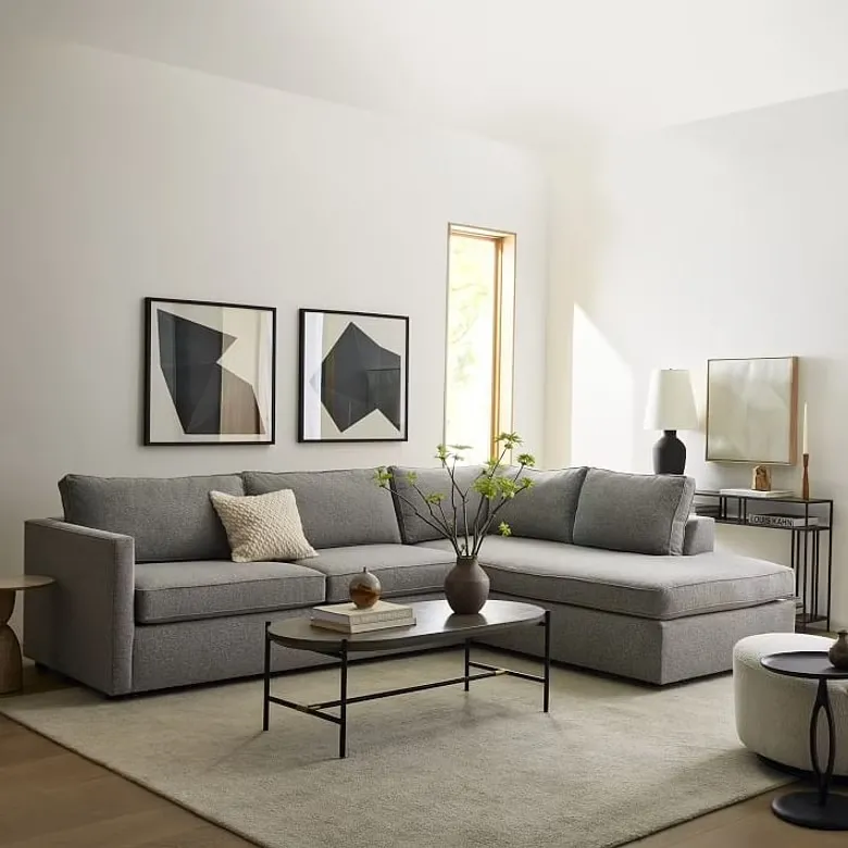 grey sleeper sofa with storage, olive grey carpet, wooden oval centre table , white walls, books on the table, paintings hanging on the wall, cushions
