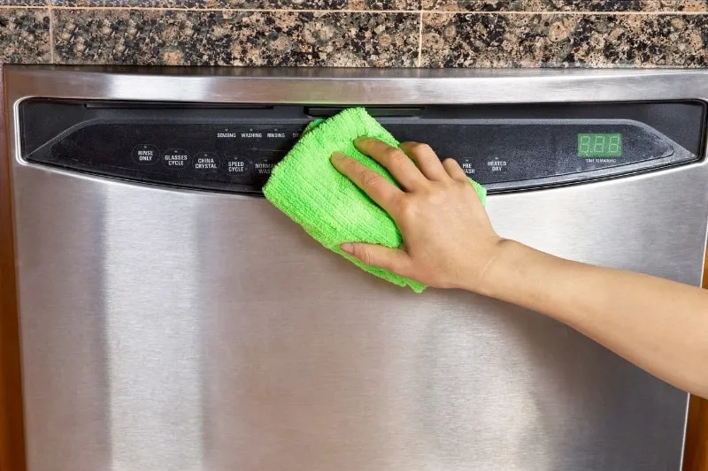 Cleaning the exterior of a dishwasher with a damp cloth.