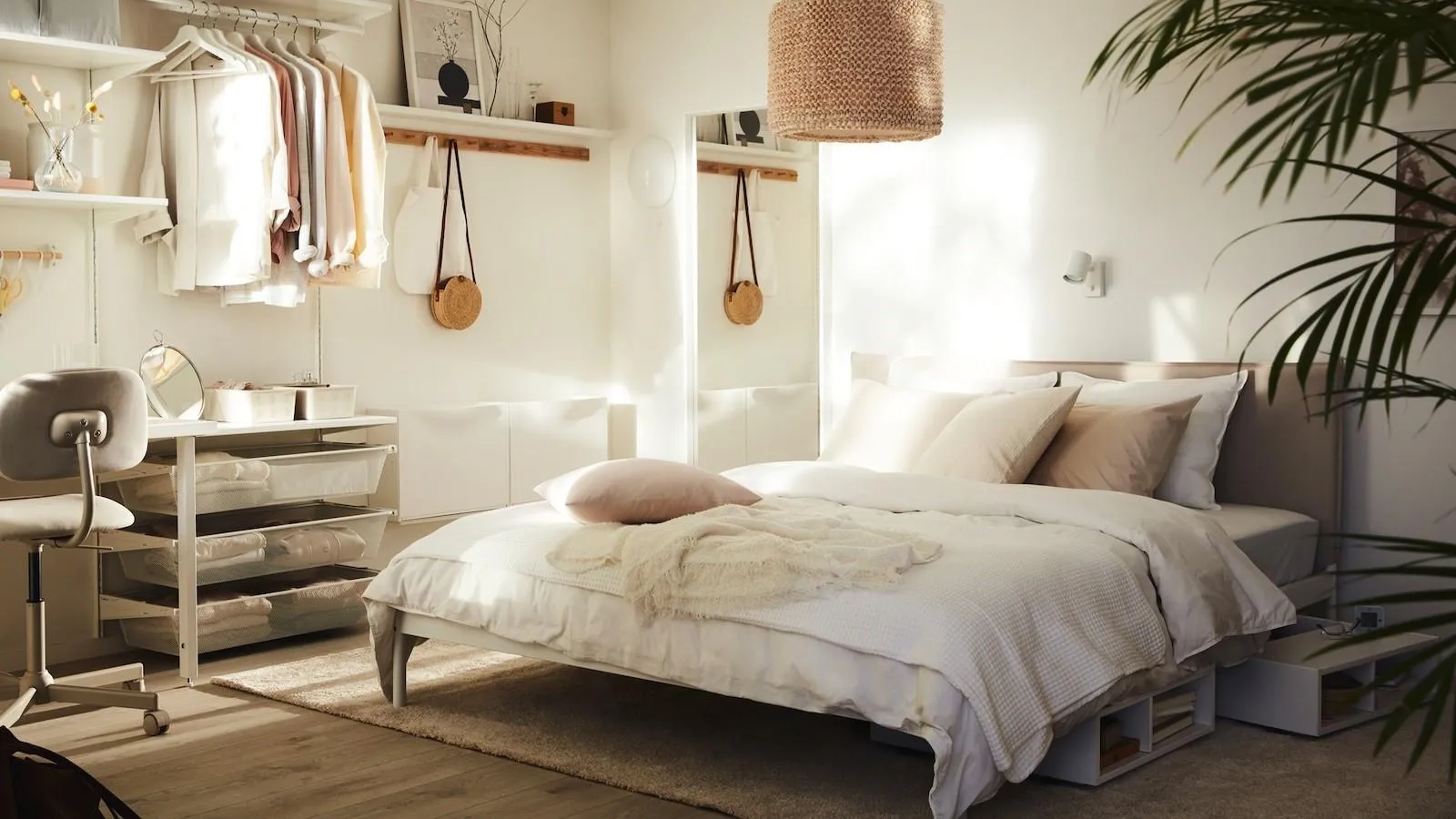 white bedroom with bed, shelf, brown pendant light, chair, table, mirror, plants and rug