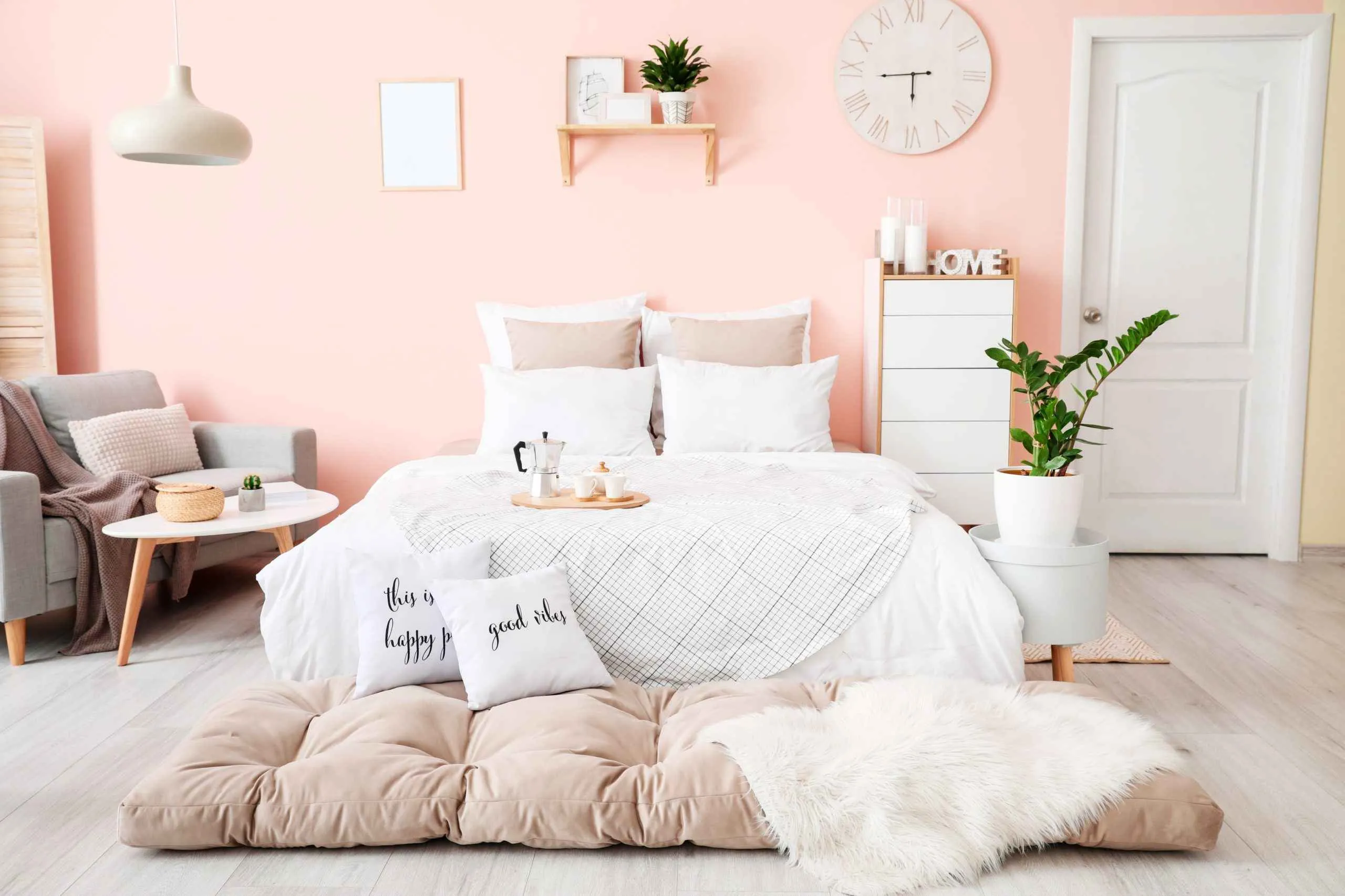 peach bedroom with white bed, grey chair, white cabinet, plants and pendant light