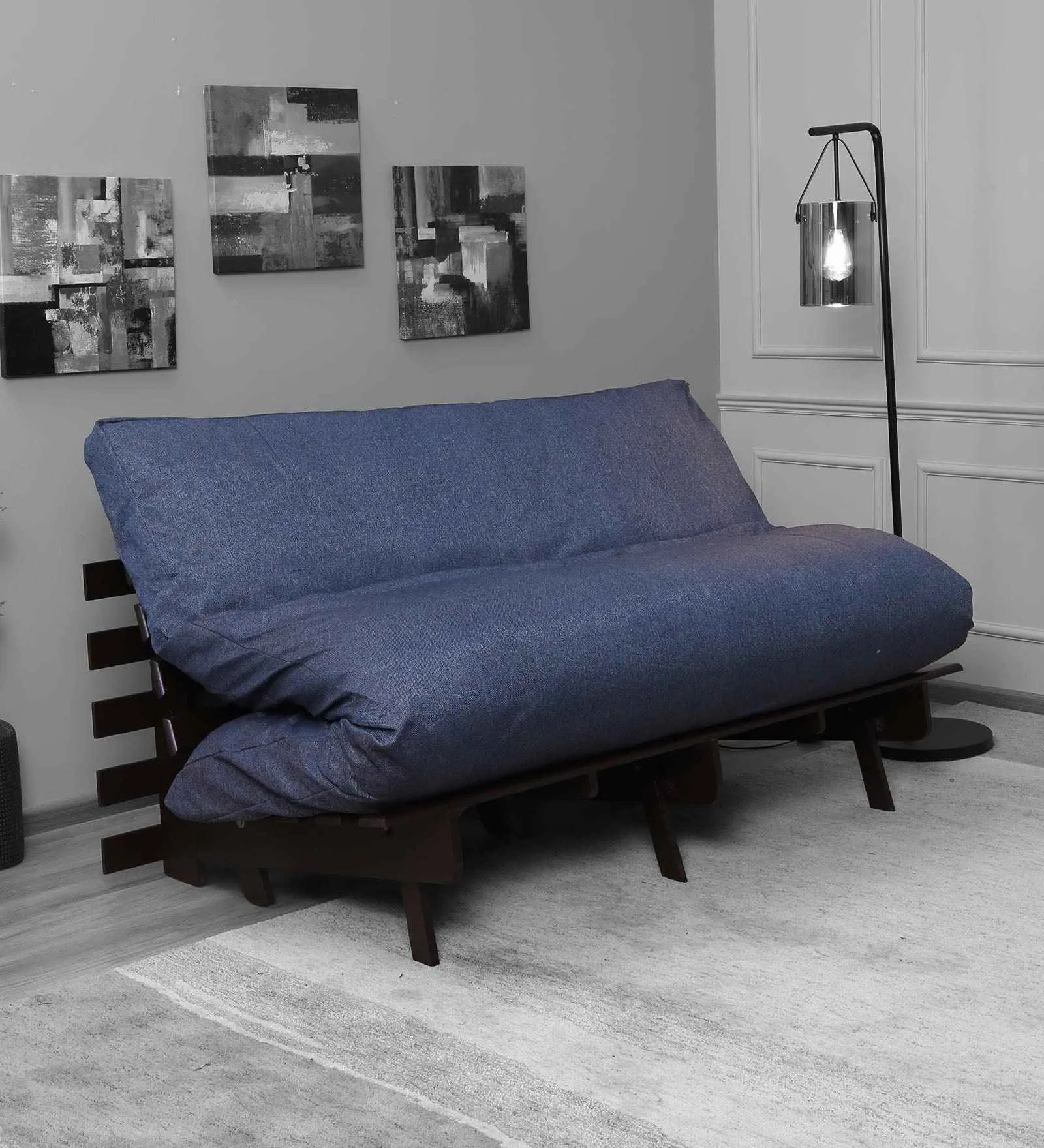blue futon sofa in a living room with floor lamp and wall art