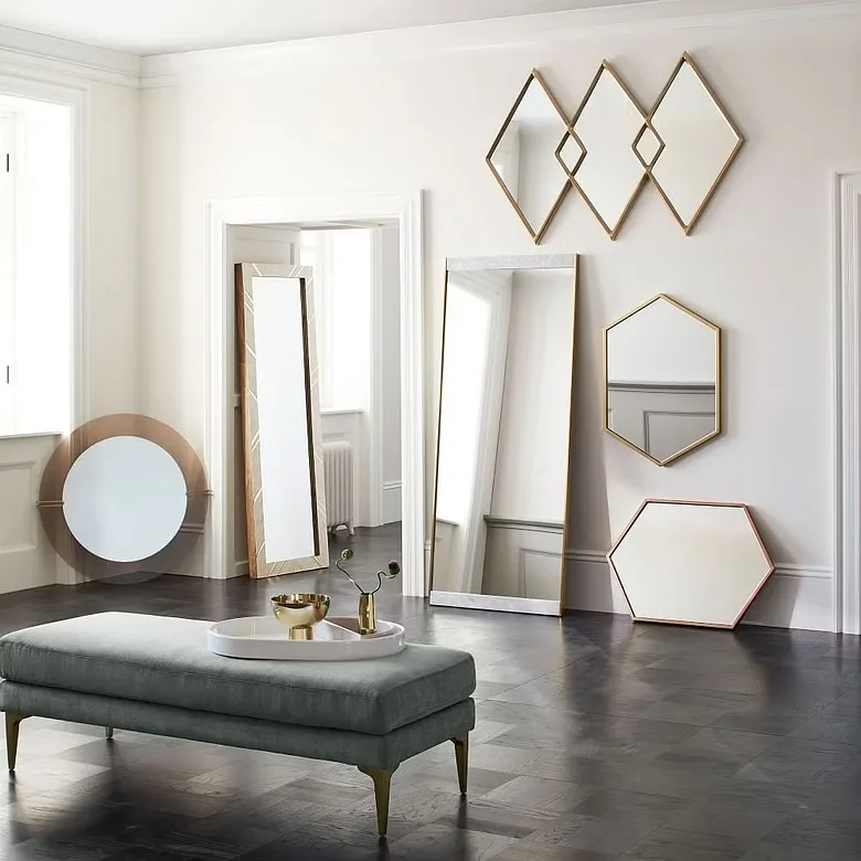 stunning overlapping and unique mirror design for walls, white walls, different mirror shapes with golden frame, a tufted bench in the middle of the room