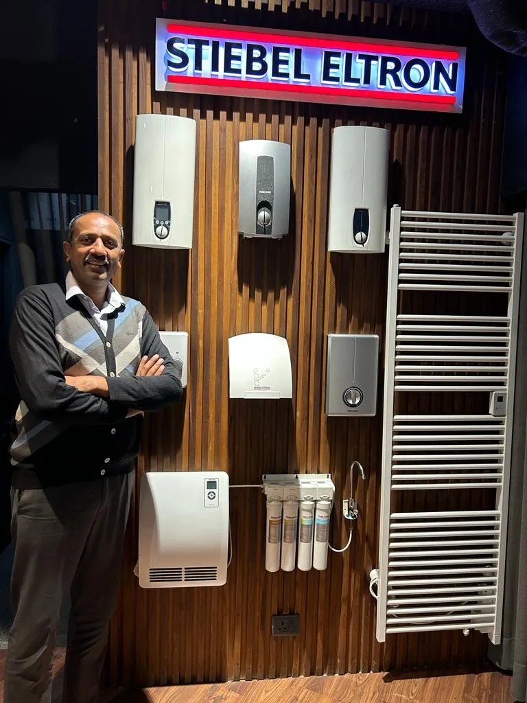 Mr. Pankaj Jain of Stylish Baths a bathroom fittings and sanitary ware dealer in Ludhiana standing in front of Stiebel Eltron brown display wall at a showroom